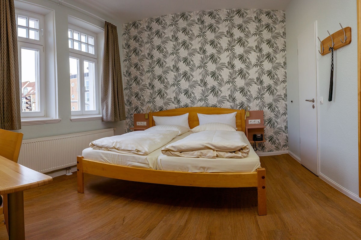 Ein Schlafzimmer mit einem hölzernen Bett, einem Nachttisch, einer Lampe und einem Fenster mit Vorhängen.