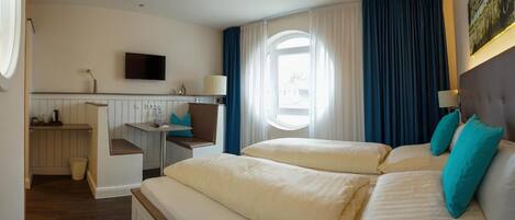 A hotel room with a bed, a desk, a chair, a TV, and a window with curtains.