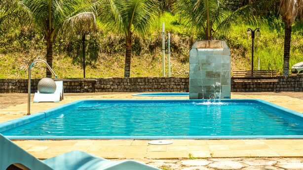 Une piscine bordée de pierres, un fauteuil de relaxation et un mur de pierres agrémenté d’un élément décoratif aquatique.