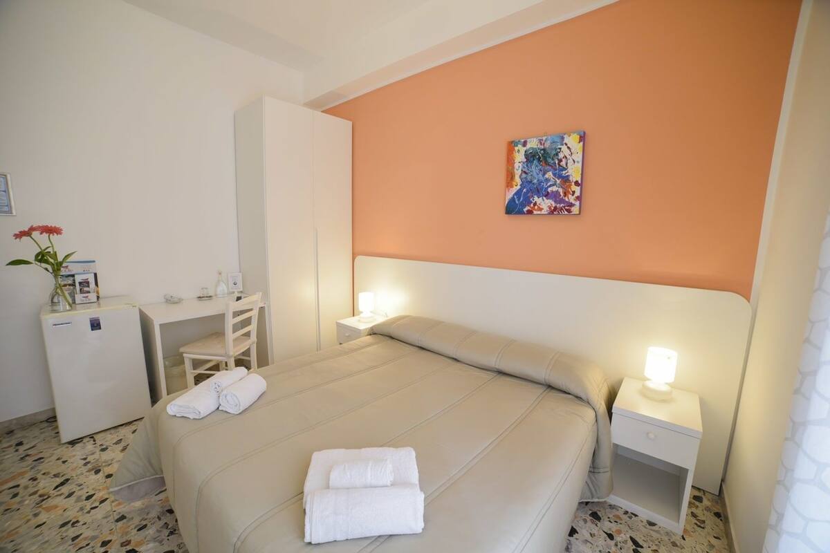 Ein Hotelzimmer mit Bett, Nachttischen, einem Schreibtisch, einem Kleiderschrank und einem Bild an der Wand.