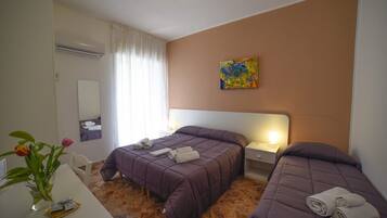 Camera d'albergo con due letti, una scrivania, una sedia, un vaso con fiori e un quadro appeso al muro.