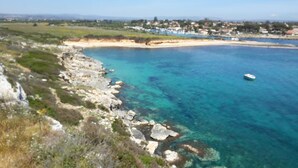 A coastal landscape with clear blue waters, rocky shoreline, and a distant town. - B&B Siracusa Holidays (Syracuse)