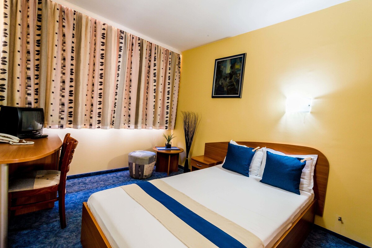 Ein Hotelzimmer mit Bett, Schreibtisch mit Computer, Stuhl, kleinem Tisch und Lampe.