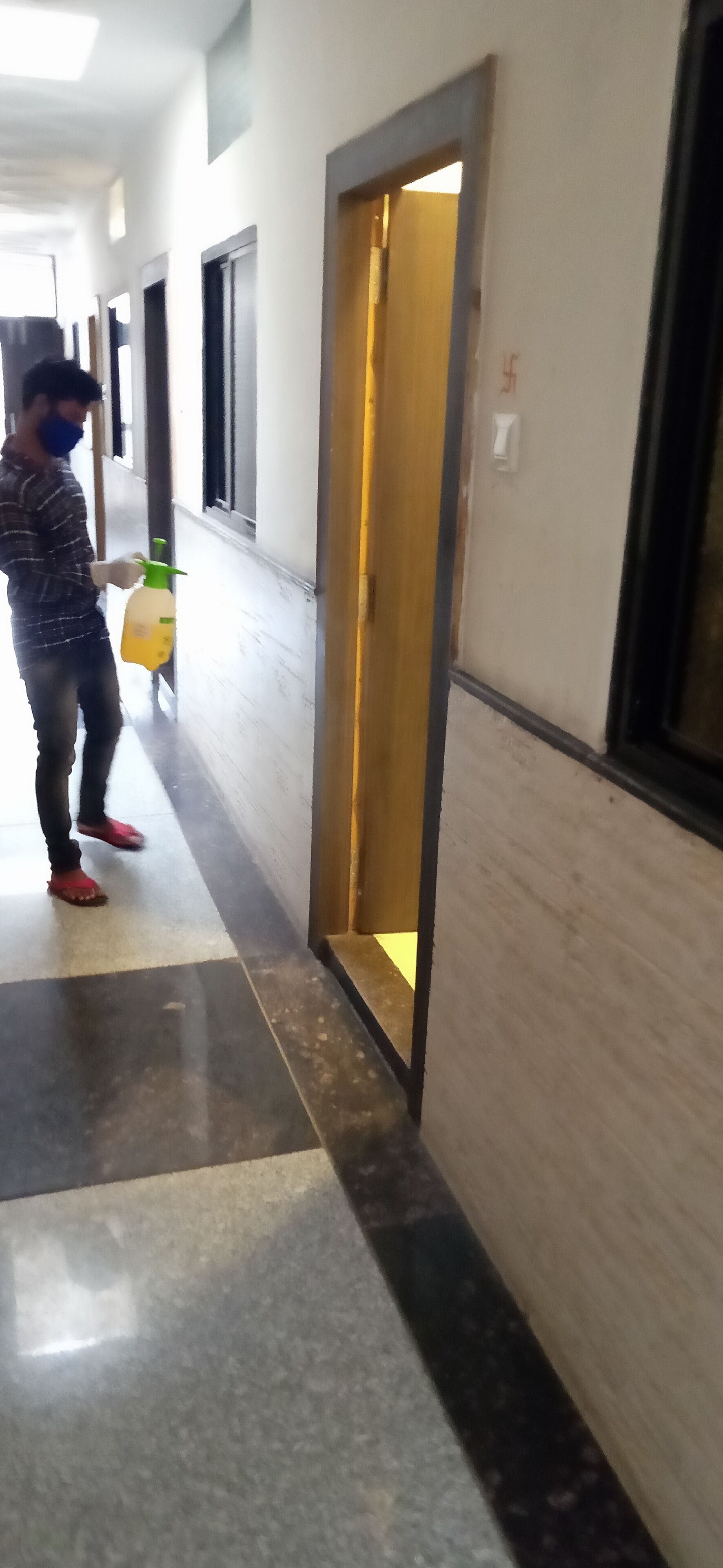 A corridor with a person holding a yellow spray bottle, a door with a golden frame, and a tiled floor.