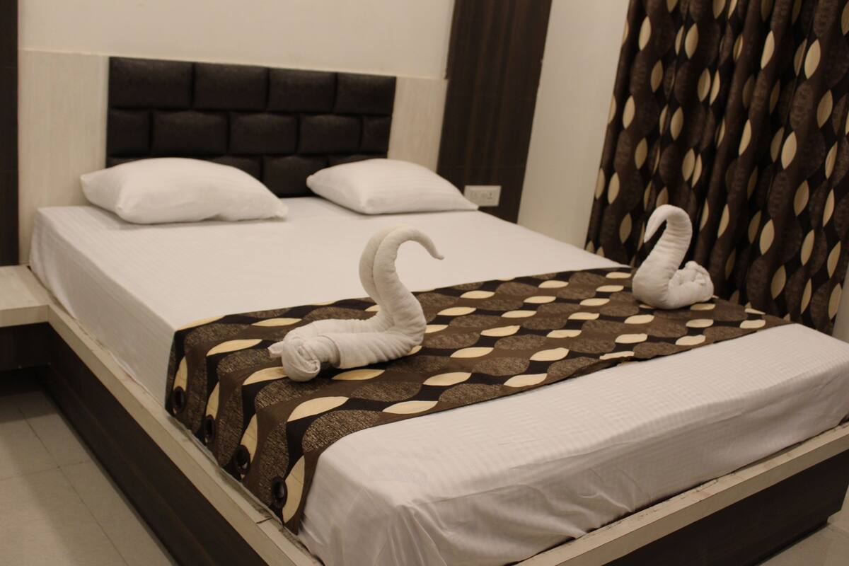 Una cama bien hecha con una colcha estampada y dos toallas con forma de cisne.