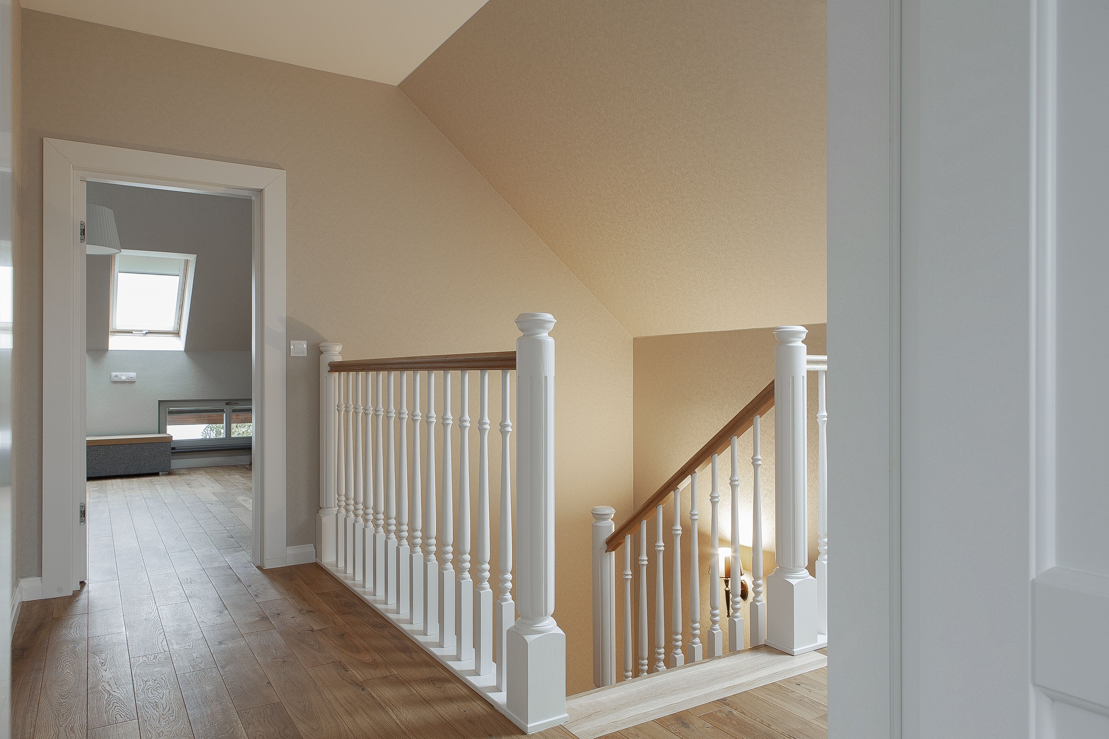 A hallway with a wooden floor, white railings, and a sloped ceiling.