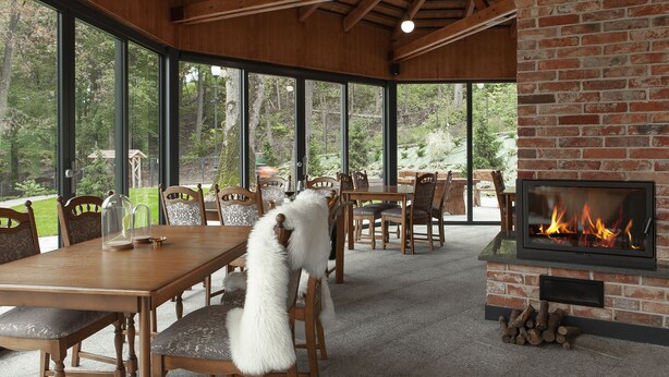A dining area with a brick fireplace, wooden furniture, and large windows overlooking a garden. - Leśny Dwór (Suleczyno)