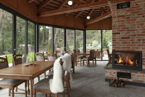 A dining area with a brick fireplace, wooden furniture, and large windows overlooking a garden. - Leśny Dwór (Suleczyno)