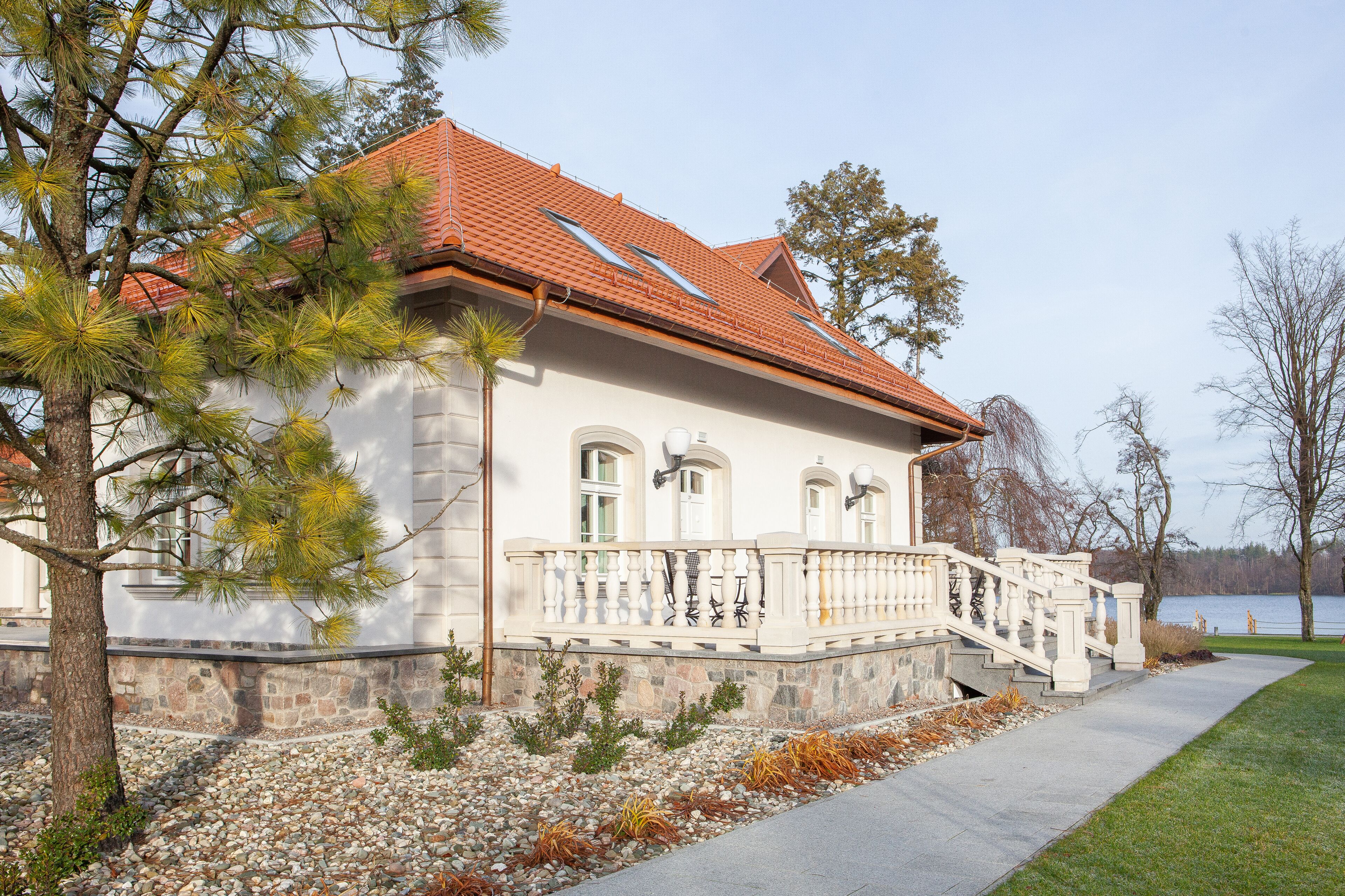A two-story house with a red-tiled roof, a stone foundation, and a white exterior.