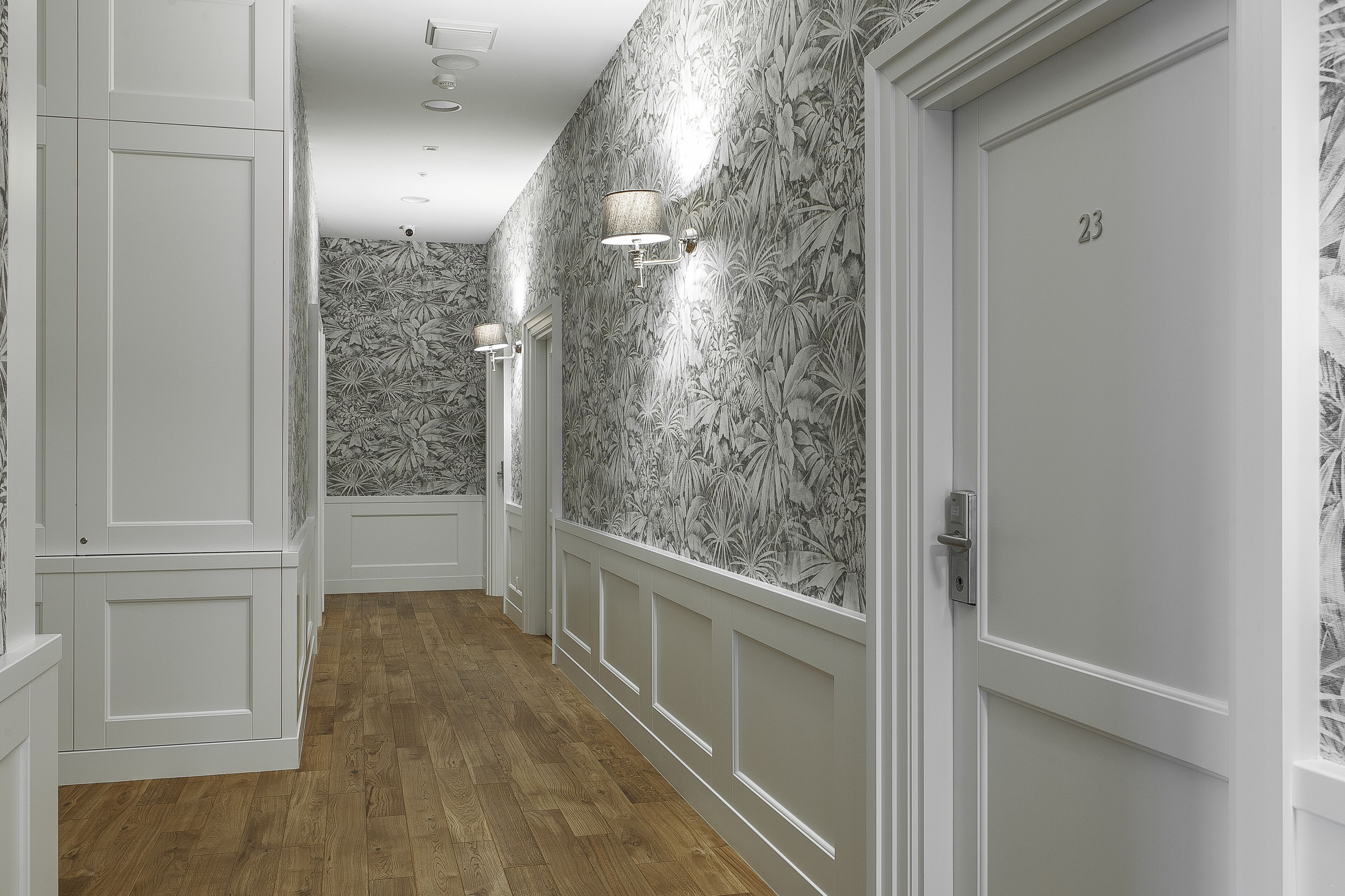 Un couloir avec un papier peint à motifs, un plancher en bois et une porte portant le numéro 23.