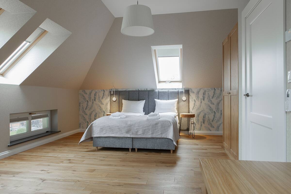 A bedroom with a sloped ceiling, a skylight, a bed with a headboard, a bedside table, and a wardrobe.