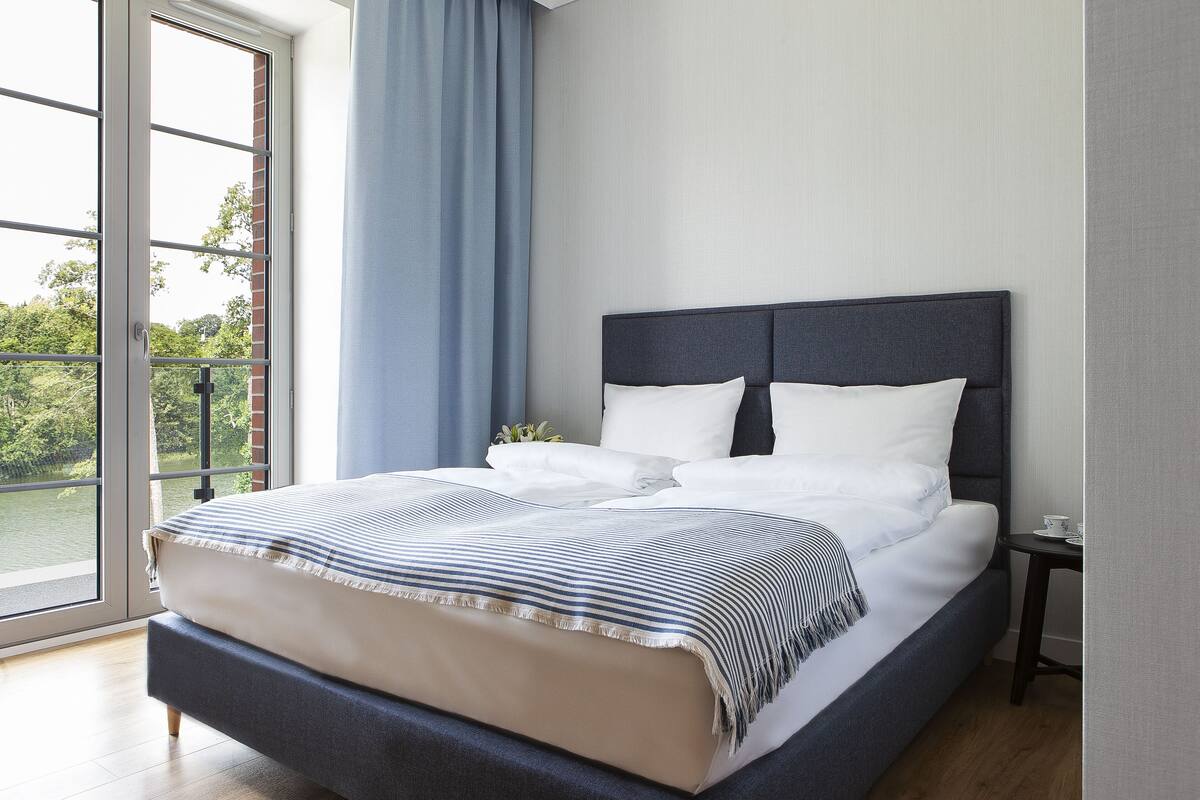 A neatly made bed with a striped blanket, a dark headboard, and a small bedside table with a cup and saucer.