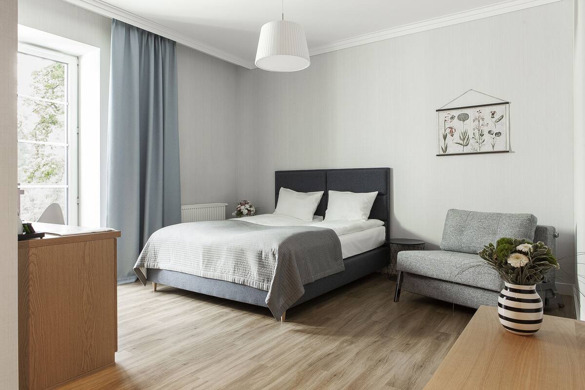 A modern bedroom with a bed, a grey sofa, a wooden desk, and a wall-mounted plant.