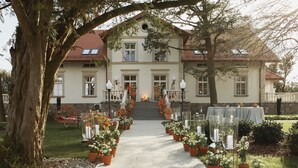A grand house with a central staircase, surrounded by potted plants and outdoor seating. - Leśny Dwór (Suleczyno)