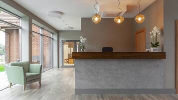 A reception area with a wooden reception desk, two hanging pendant lights, and a green armchair.