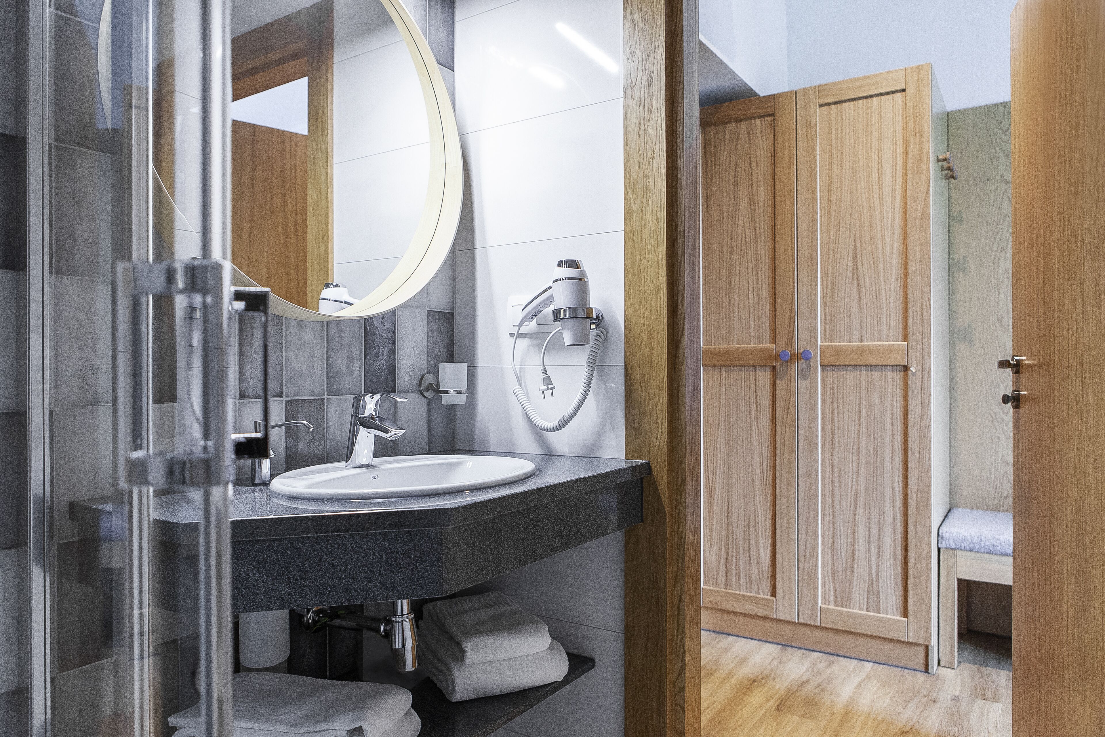 Ein modernes Badezimmer mit Duschkabine aus Glas, einem weißen Waschbecken und einem Badmöbelkorpus aus Holz.