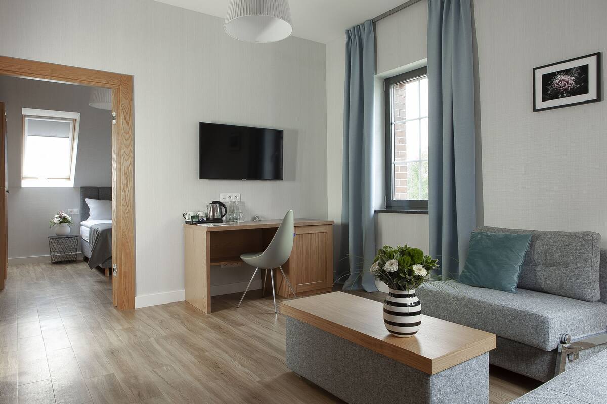 A modern living room with a wooden desk, grey sofa, and a flat-screen TV mounted on the wall.