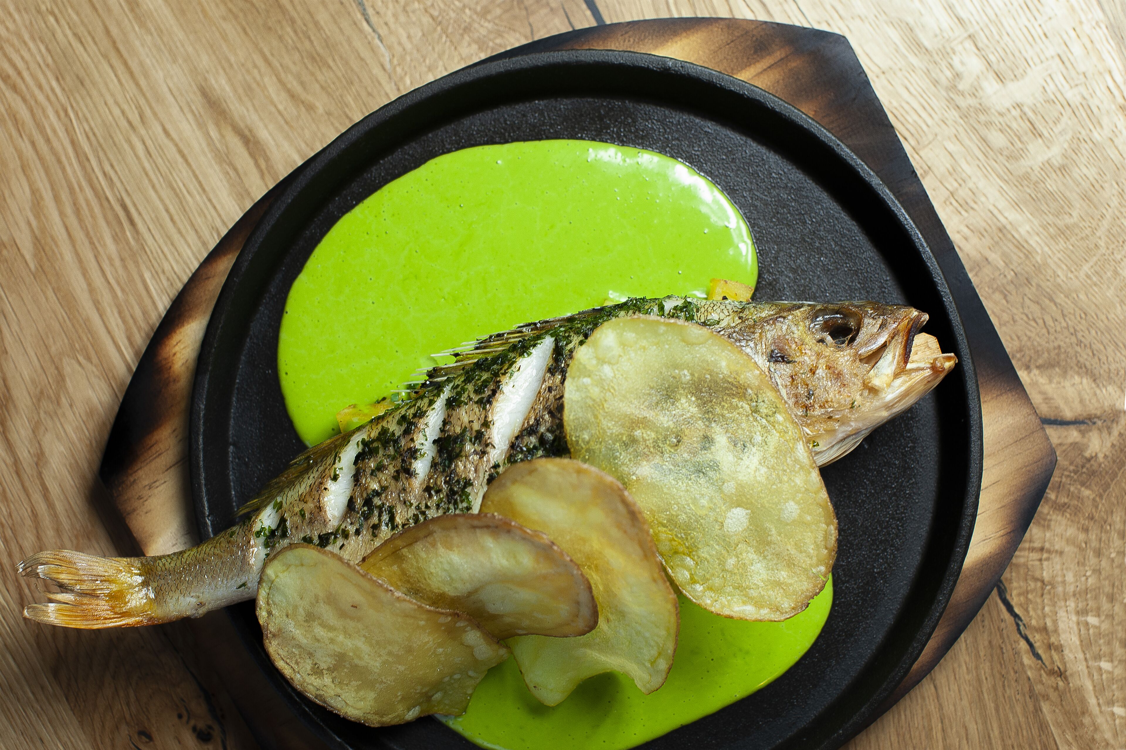 Peixe com batatas fritas em um prato preto com molho verde.