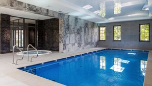 An indoor swimming pool with a clear view of the ceiling, a brick wall, and a glass door leading to another room. - Leśny Dwór (Suleczyno)