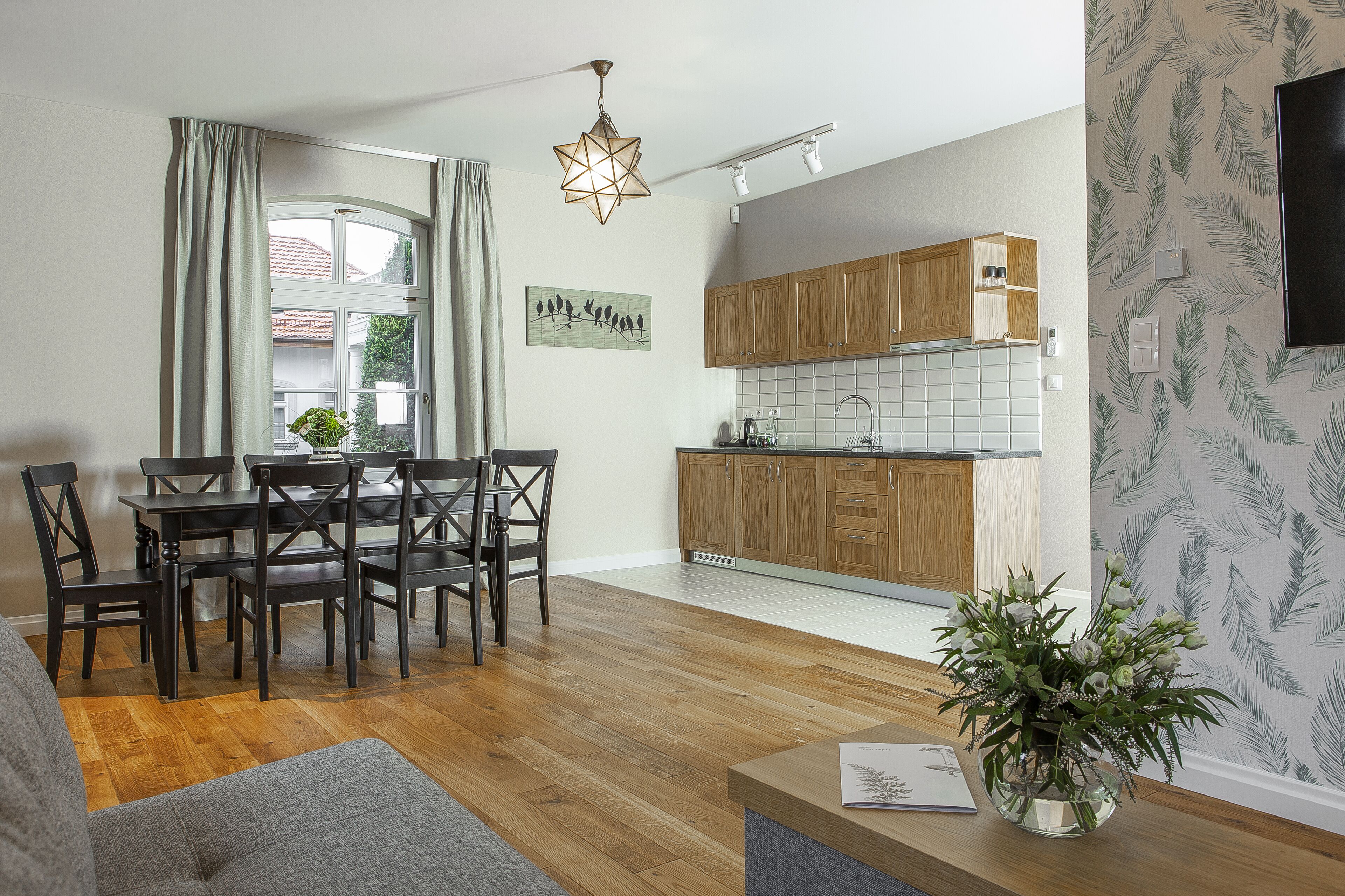 Une cuisine moderne avec des meubles en bois, un coin repas avec une table et des chaises, et un salon avec un canapé et une plante.