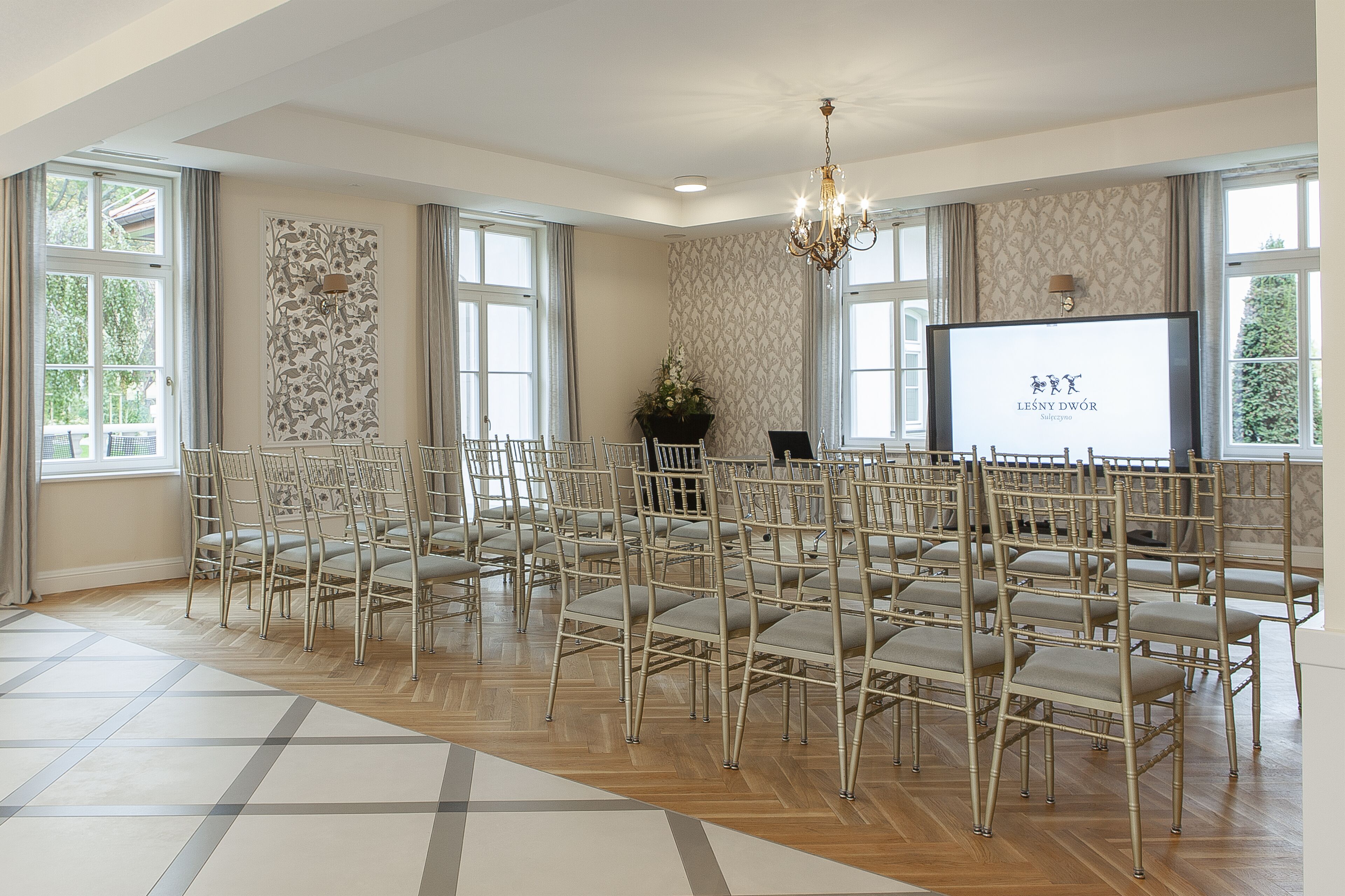 A conference room with rows of chairs, a projector screen, and a chandelier.