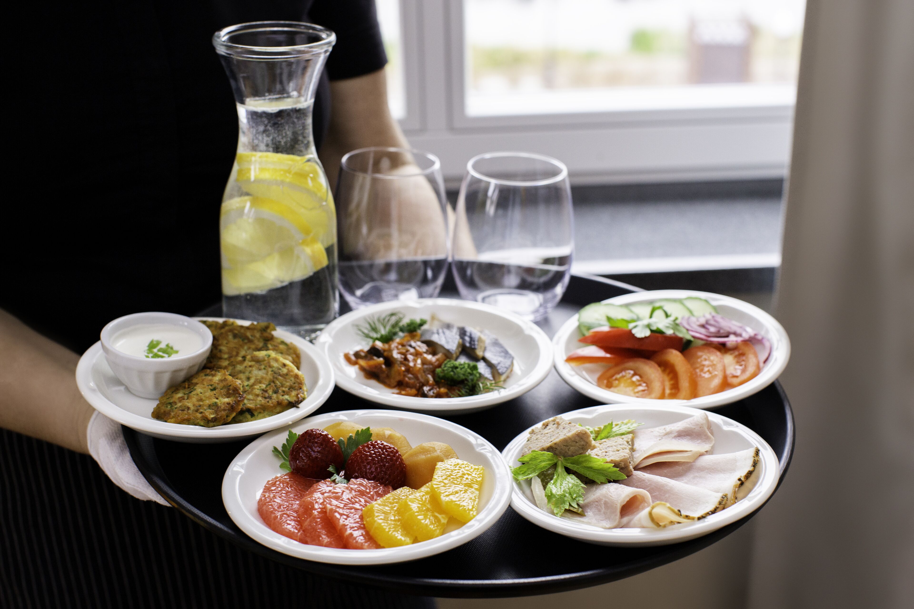 A tray with various dishes including a salad, fruit, and a meat dish, accompanied by a glass of juice and water.
