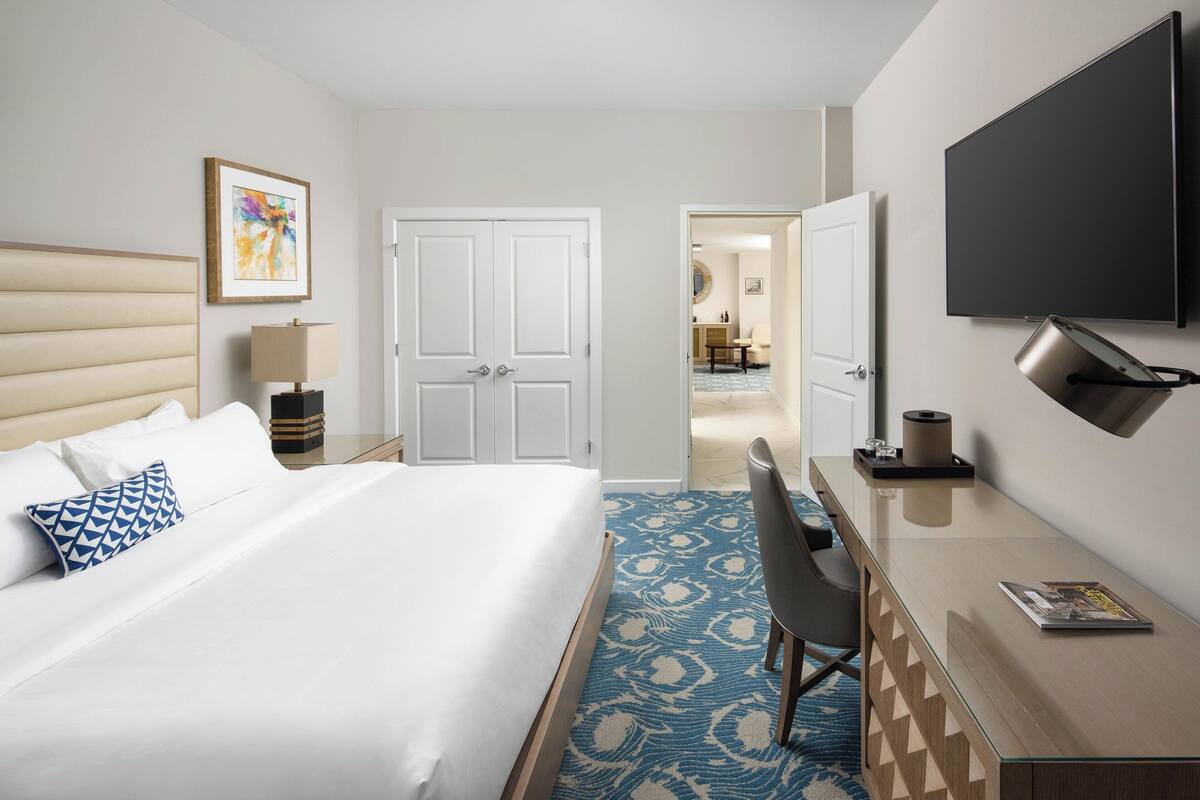 Une chambre d’hôtel équipée d’un lit, d’un bureau, d’une télévision et d’une porte donnant sur une salle de bain.