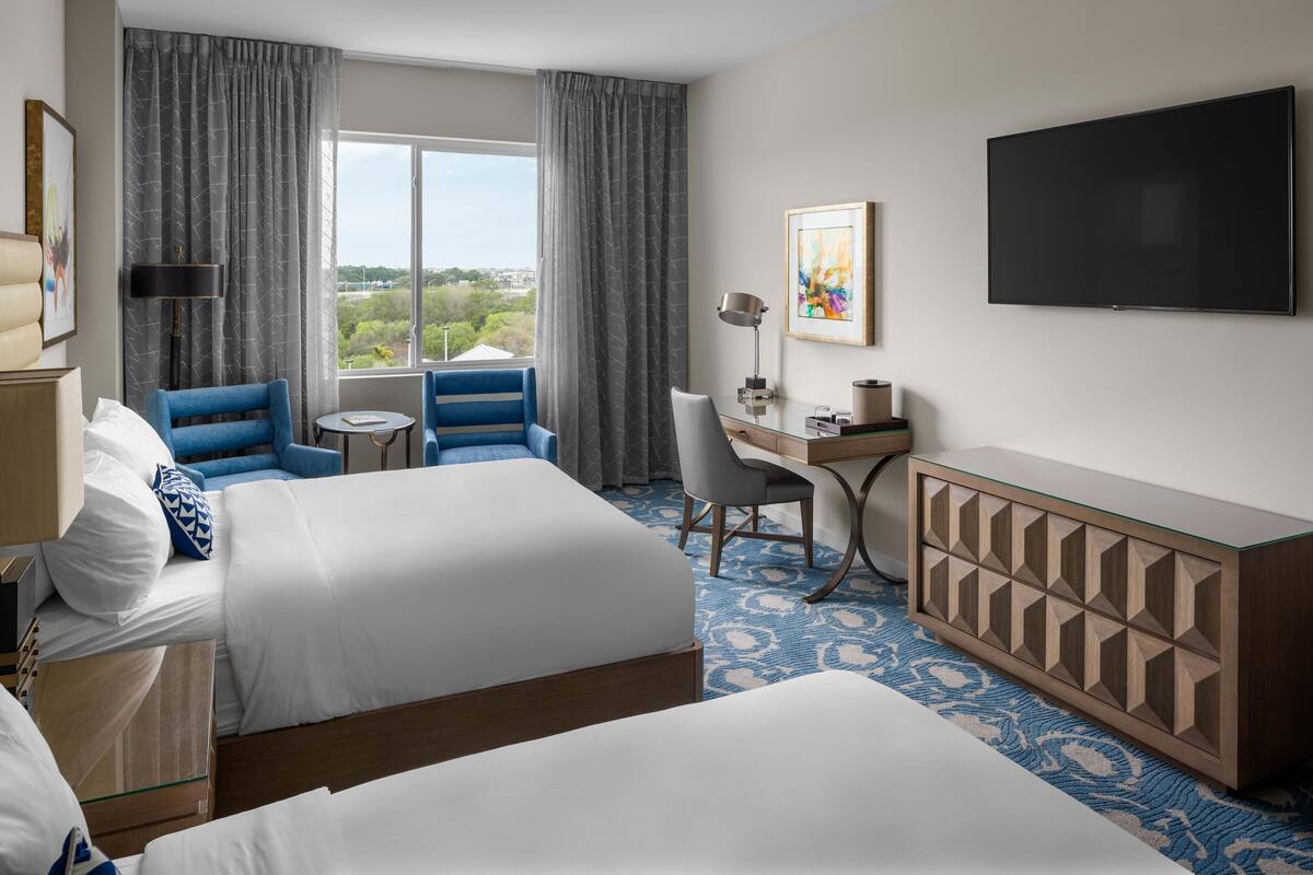 Une chambre d’hôtel avec deux lits, un bureau, une chaise, une télévision et une vue sur l’extérieur.