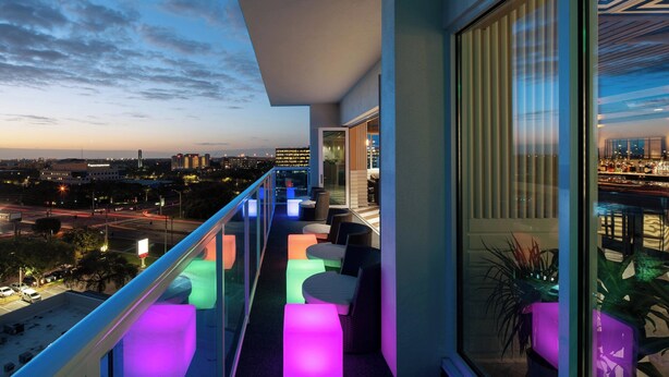 Varanda com iluminação colorida, espaço para sentar e vista para a cidade.