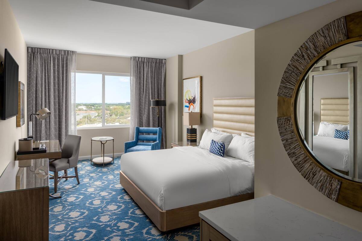Une chambre d’hôtel avec un grand lit, un bureau, une chaise et une vue sur l’extérieur.