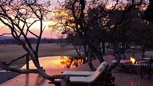 A sunset view from a deck with lounge chairs and a fire pit. - Zangarna Game Lodge (Vaalwater)