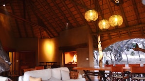A cozy indoor setting with a fireplace, wooden furniture, and a thatched roof. - Zangarna Game Lodge (Vaalwater)