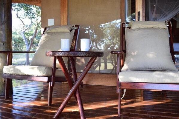 Una terraza de madera con dos sillas de madera y una mesita, cada una con un cojín.