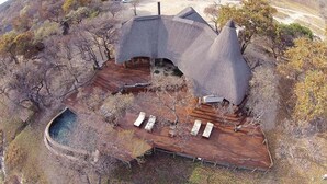 An aerial view of a thatched-roof house with a wooden deck, surrounded by trees and a small pond. - Zangarna Game Lodge (Vaalwater)