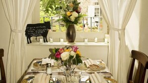 A dining table set for two with a vase of flowers and a chalkboard sign.