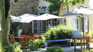 A hotel with outdoor seating, stone walls, and hanging flower baskets.