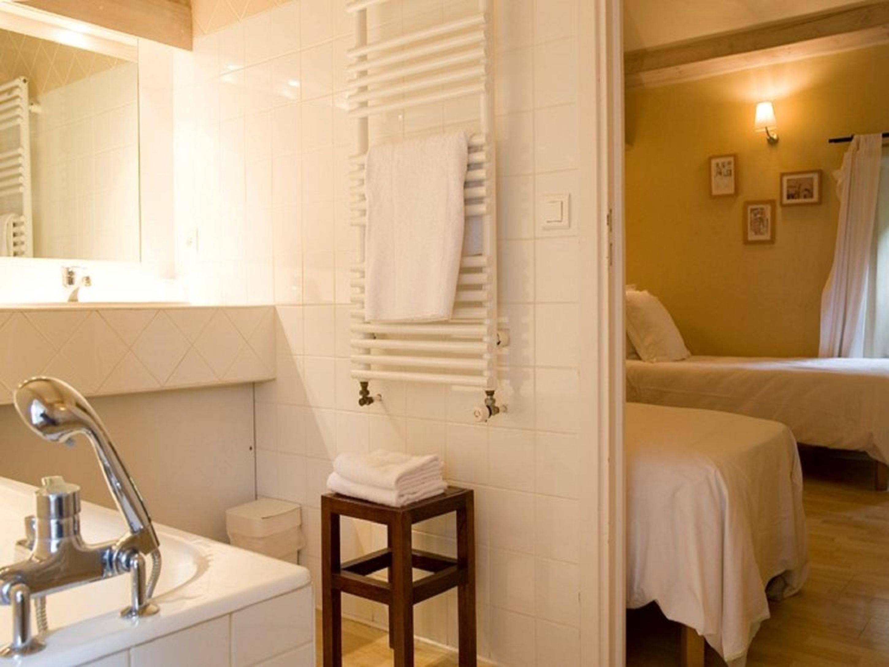 A hotel bathroom with a sink, mirror, towel rack, and a wooden stool.