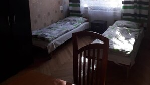A room with two single beds, a wooden table, a chair, a wardrobe, and a window with striped curtains. - Hostel mPark Chorzow (Chorzow)