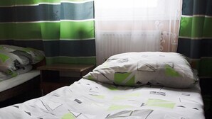 Ein Einzelbett mit weiß-grüner Bettdecke, einem weißen Kissen und einem grün-weißen Streifenvorhang.