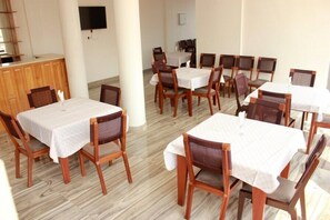 A dining area with multiple tables and chairs, a wooden counter, and a flat-screen TV mounted on the wall.