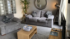 A living room with two grey sofas, a coffee table, a potted plant, a mirror, and a tripod. - Harbour View Luxury Comfortable Holiday Apartment (Donaghadee)