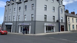 A multi-story building with a grey facade, two coffee shops on the ground floor, and a red car parked on the street. - Harbour View Luxury Comfortable Holiday Apartment (Donaghadee)