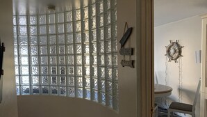 A room with a large window with frosted glass panels, a small table with a chair, and a wall-mounted ship's wheel decoration. - Harbour View Luxury Comfortable Holiday Apartment (Donaghadee)