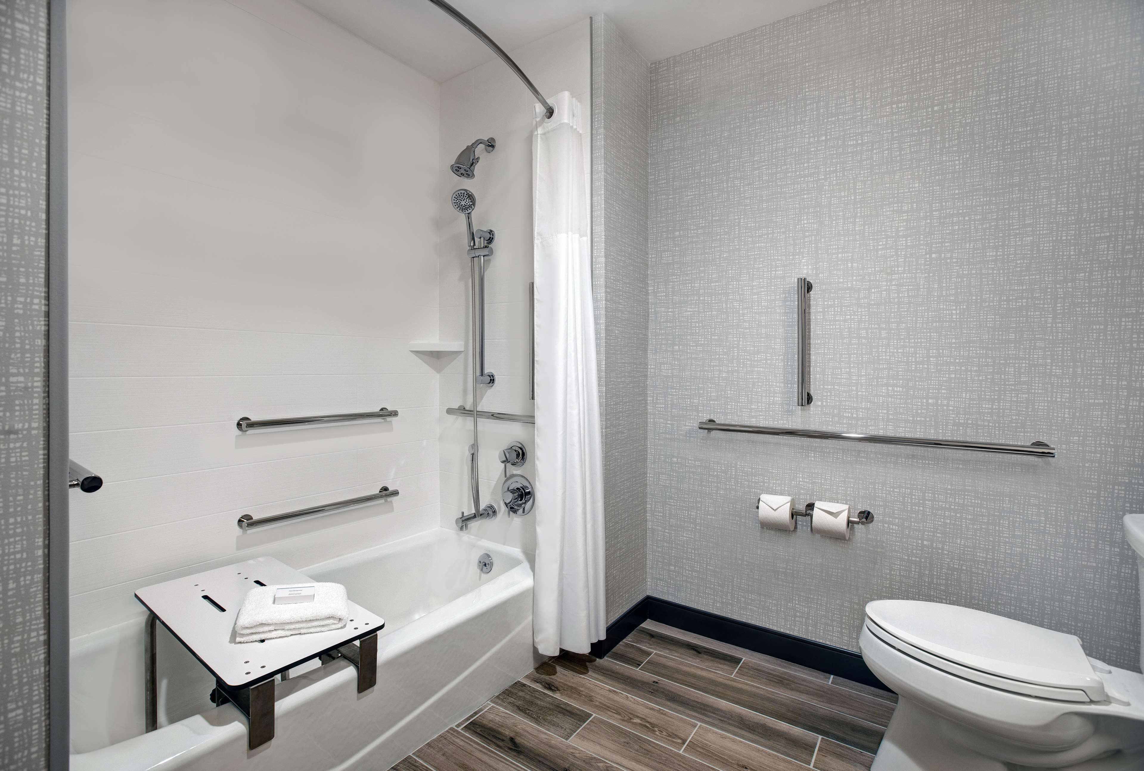 Un baño moderno con cabina de ducha, barras de apoyo, inodoro y tocador pequeño con una toalla.