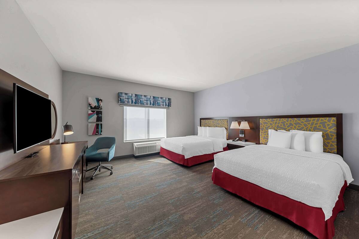 A hotel room with two beds, a desk, a TV, and a window.