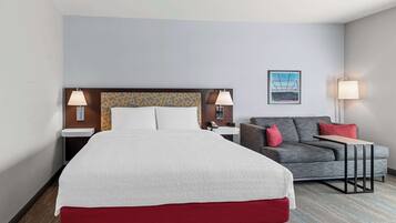 A hotel room with a large bed, a grey sofa, two bedside tables with lamps, and a framed picture on the wall.