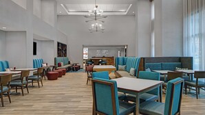 A spacious indoor area with multiple seating arrangements including tables and booths, a central reception area with a 'WELCOME' sign, and a modern ceiling design. - Hampton Inn & Suites Farmers Branch Dallas (Farmers Branch)