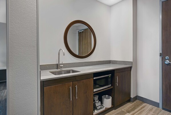 Un baño moderno con lavamanos, espejo y horno microondas integrado.