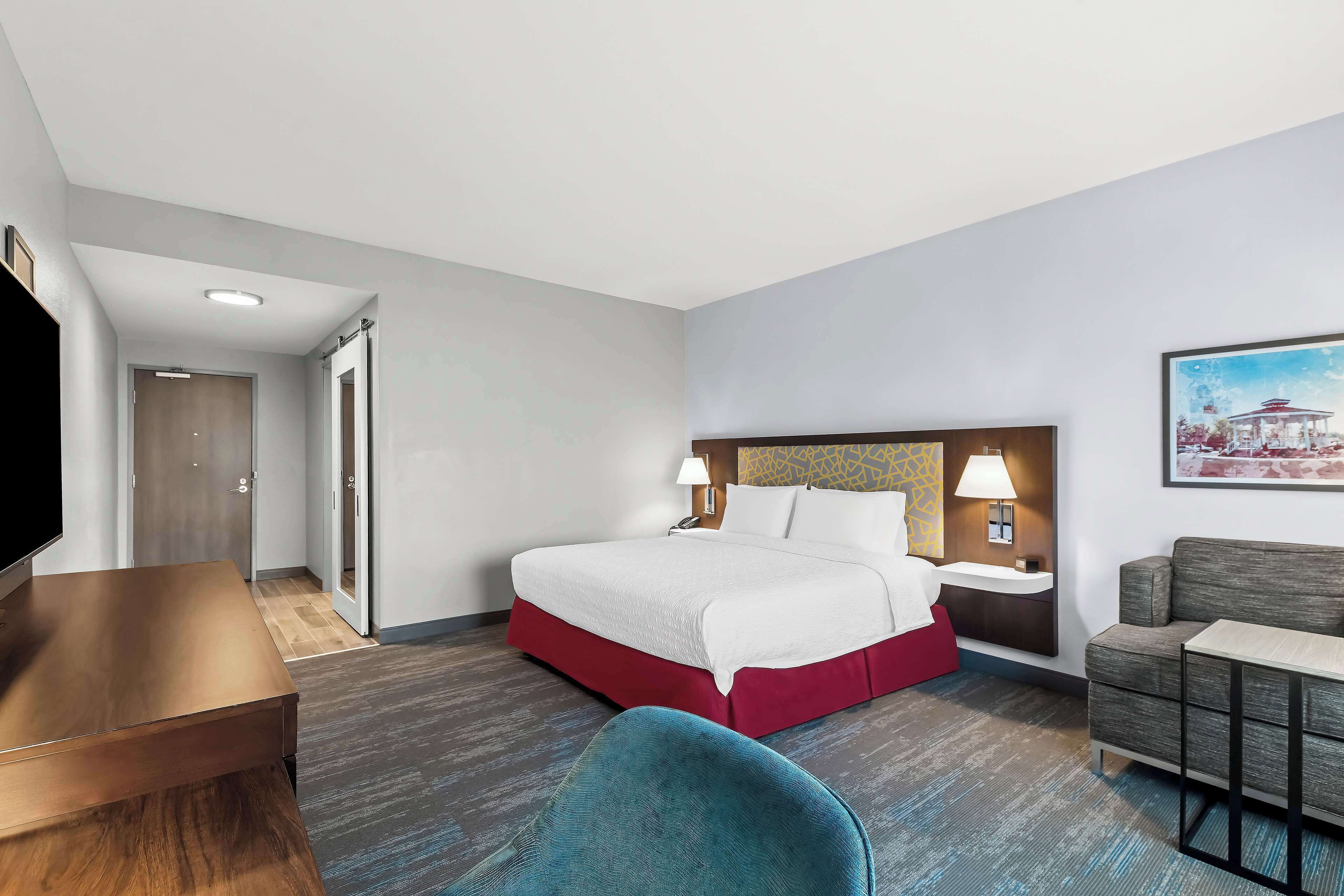 A hotel room with a bed, bedside tables, a desk, a chair, and a TV.