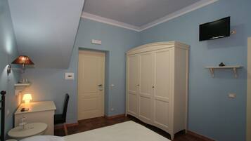 Un dormitorio con cama, mesita de noche, lámpara, armario y televisor montado.